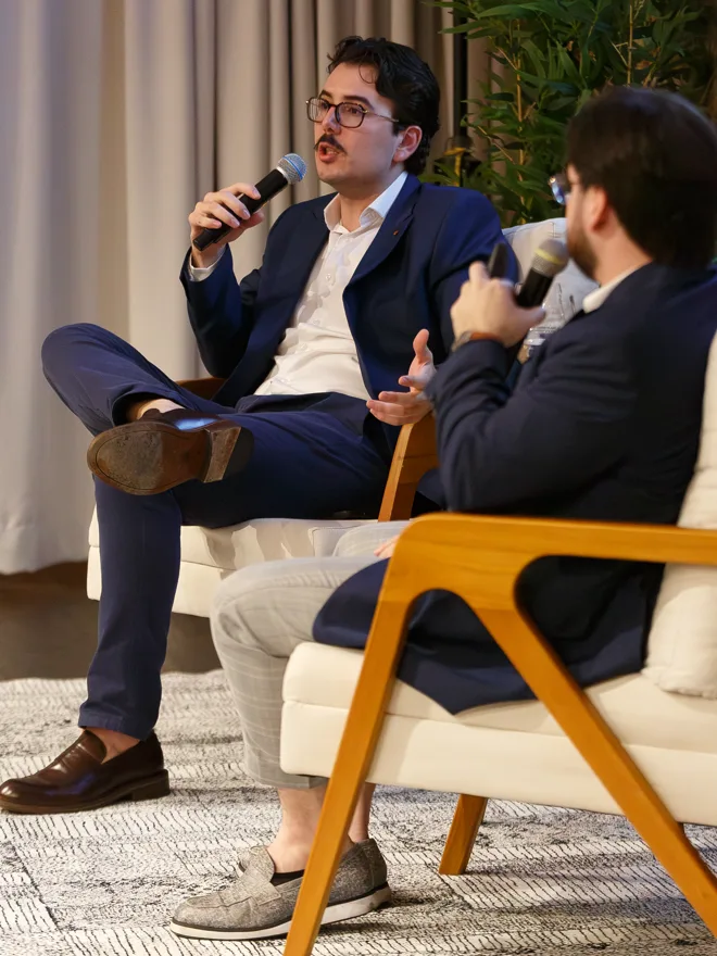 Gabriel Madona conversando ao microfone com outro participante, os dois sentados em poltronas